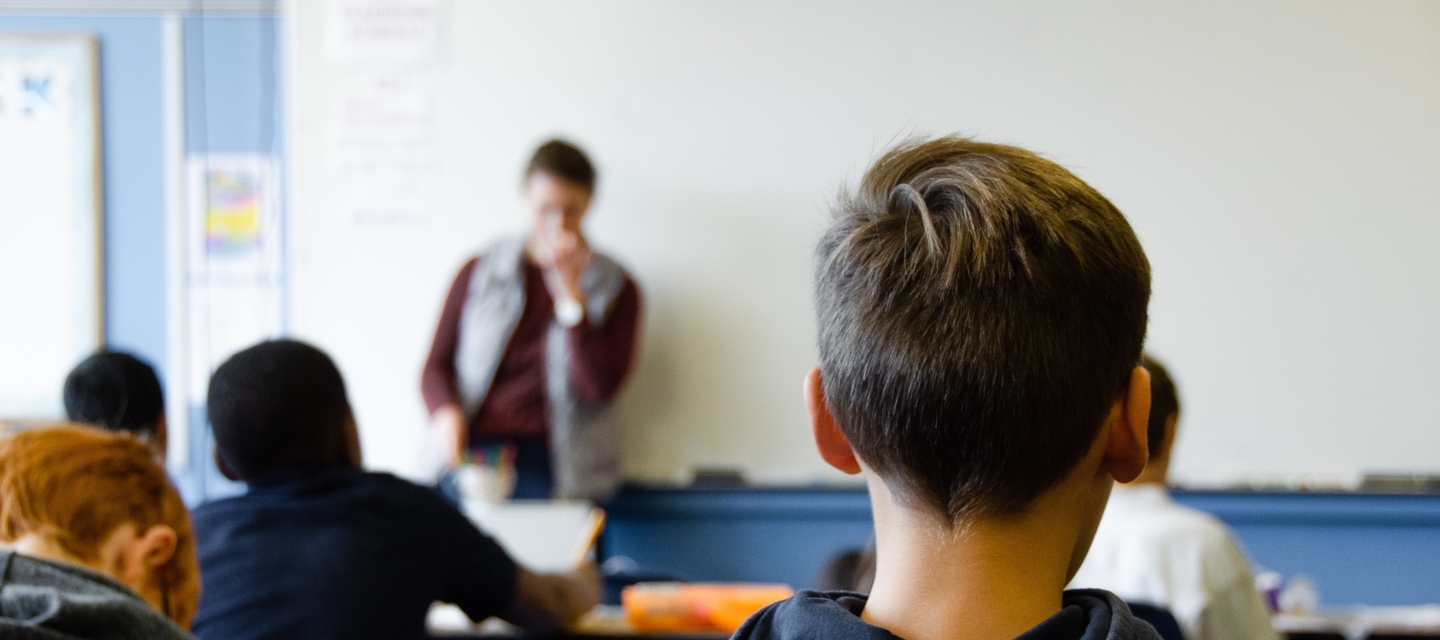 Students in classroom, teacher at front of room at whiteboard